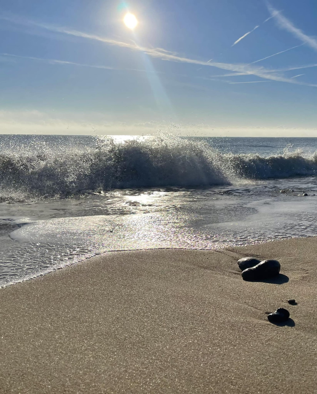 Ocean wave crashing on sandy beach with bright sun and blue sky