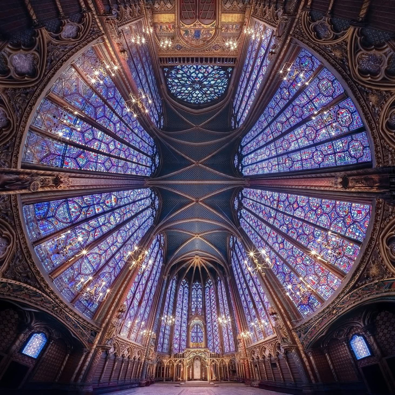 Upward view of Gothic cathedral with symmetrical stained glass windows and ornate vaulted ceiling