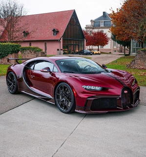 Burgundy Bugatti Chiron parked on a driveway near buildings and autumn trees