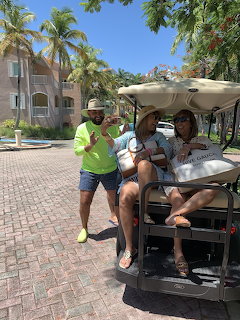 Three women posing with a golf cart on a sunny palm-lined street