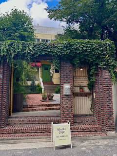 Brick building entrance covered in ivy with iron gate and cafe sign on sidewalk