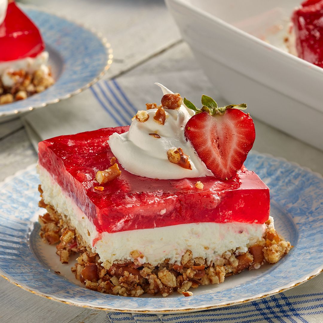 Slice of layered strawberry cheesecake with whipped cream and fresh strawberry on blue plate