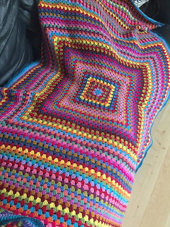 Colorful crochet granny square blanket with concentric pattern in many bright colors draped on dark sofa