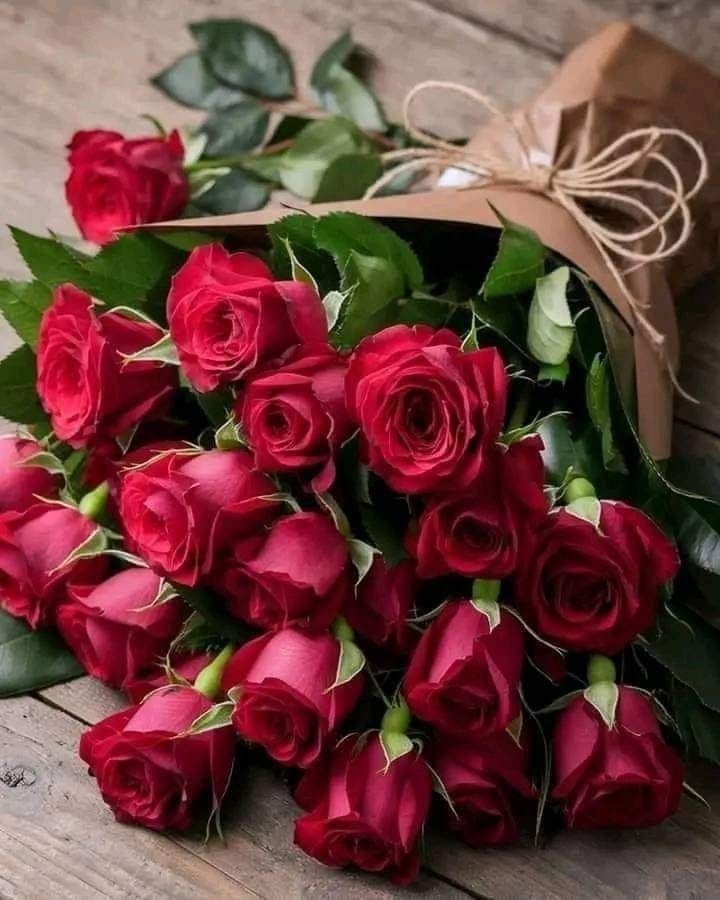 Bouquet of deep red roses wrapped in brown paper on a wooden surface