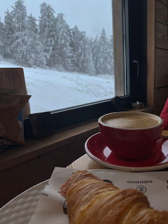 Red coffee cup and pastry on a table by a window with snowy trees outside