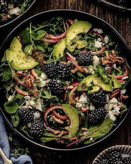 Salad bowl with blackberries, avocado slices, greens, nuts and seeds on dark wood background
