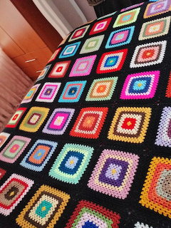 Colorful crochet granny square blanket with multicolored concentric squares on black background draped over furniture