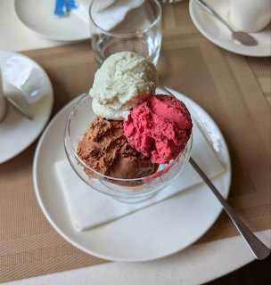 Three scoops of ice cream in vanilla, strawberry and chocolate flavors served in a glass cup on white plate