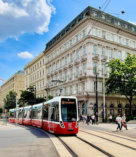 Red and white tram on tracks in front of ornate white building under blue sky with clouds