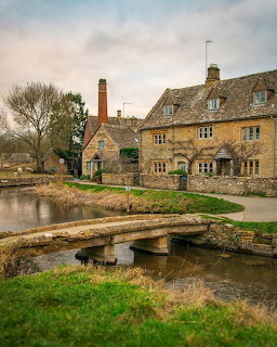 Golden stone cottages with a small stone bridge over a village pond