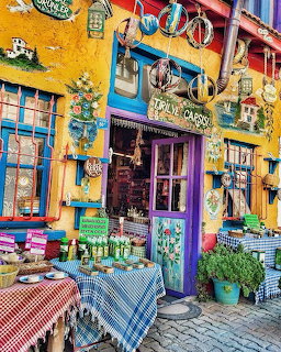 Bright yellow shop facade with blue accents, outdoor tables with checkered cloths, and colorful decorations