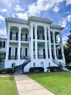 White columned antebellum plantation mansion with balconies and staircases under blue sky
