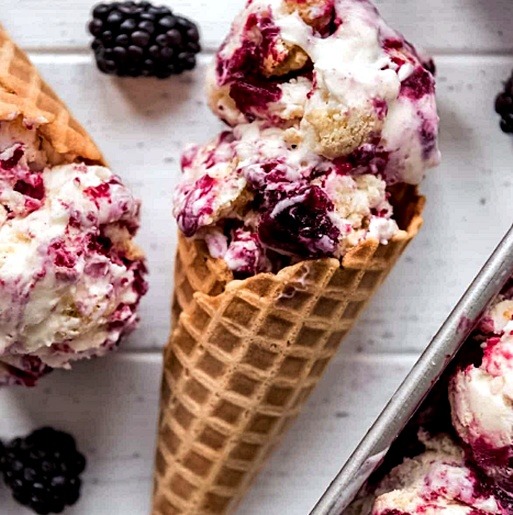 Waffle cones with blackberry swirled ice cream and fresh blackberries on white surface