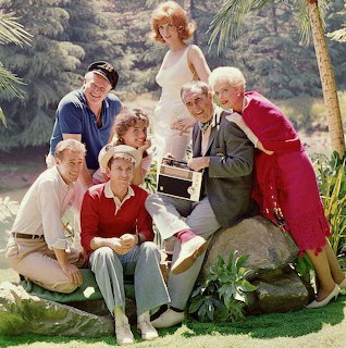 Seven people in colorful clothes pose outdoors with a portable radio in a tropical setting