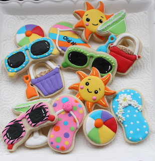 Assortment of decorated summer-themed sugar cookies on white surface including sunglasses, flip-flops, and beach balls