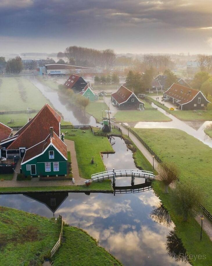 Aerial view of Zaanse Schans with traditional green Dutch houses, canal, bridge, and misty landscape