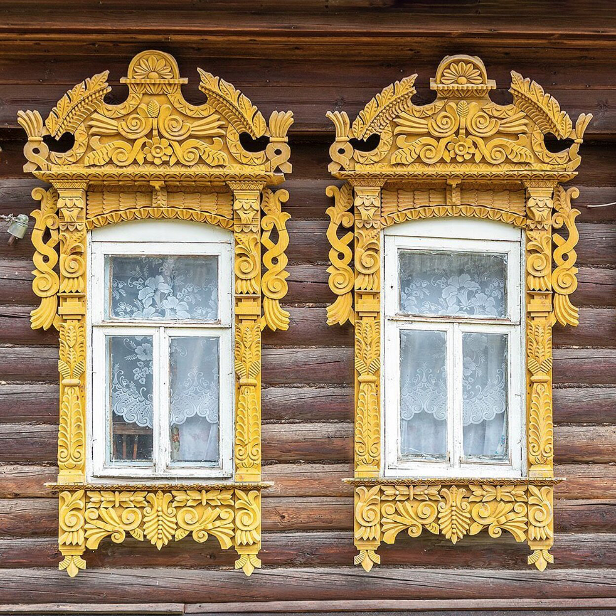 Two white windows with ornate yellow carved frames on a wooden wall