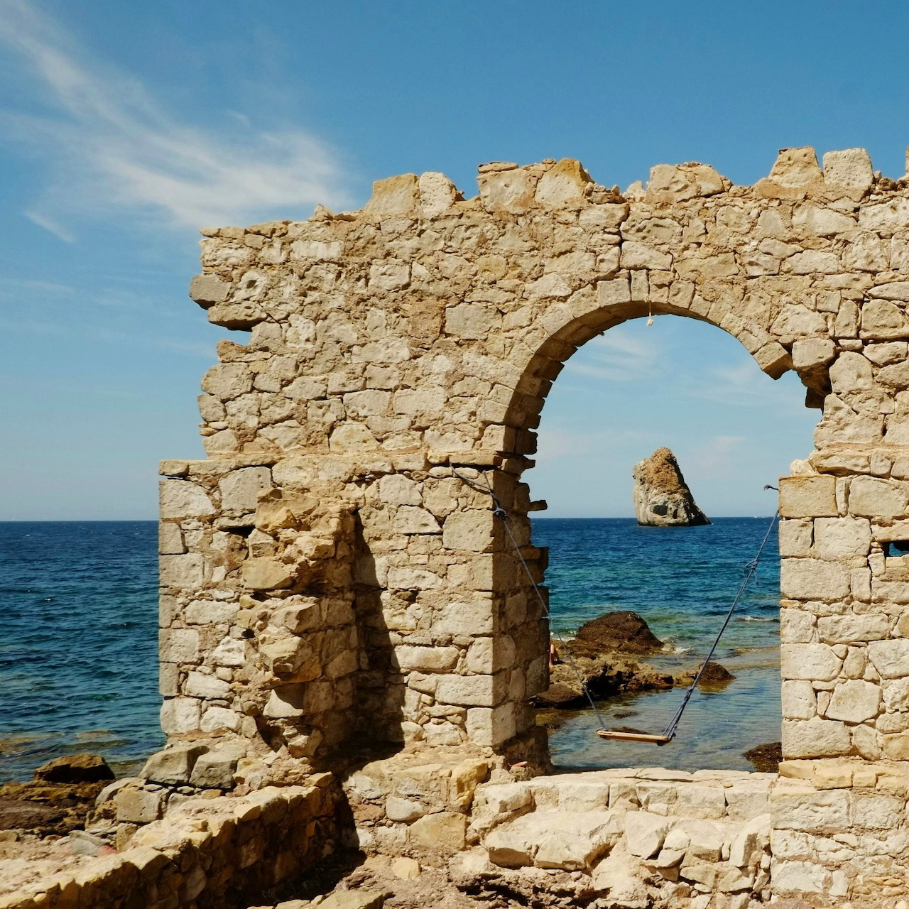 Stone arch ruins by the sea with a small swing and offshore rocks