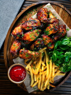 Fried chicken wings with french fries and salad on wooden plate