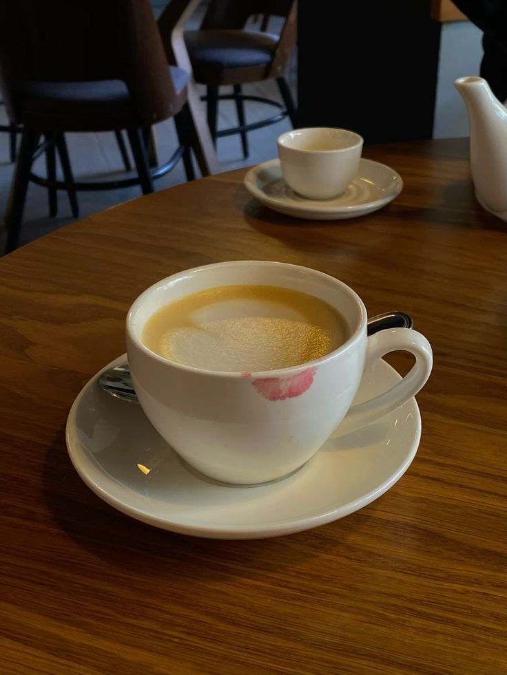 Two white coffee cups on saucers at a café table, one with a lipstick mark