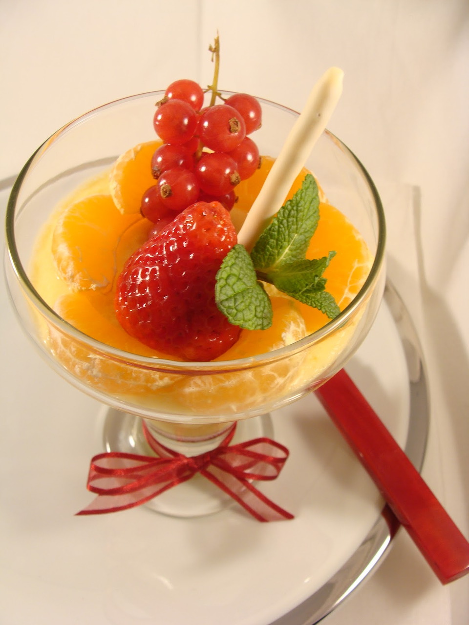 Glass dessert cup with fresh strawberries, red currants, peach slices and mint leaf garnish on white plate