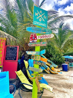 Tropical beach scene with colorful signs, palm trees, and kayaks at Maho Beach