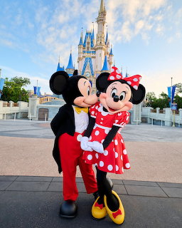 Mickey and Minnie Mouse mascots embracing in front of castle at Disney theme park
