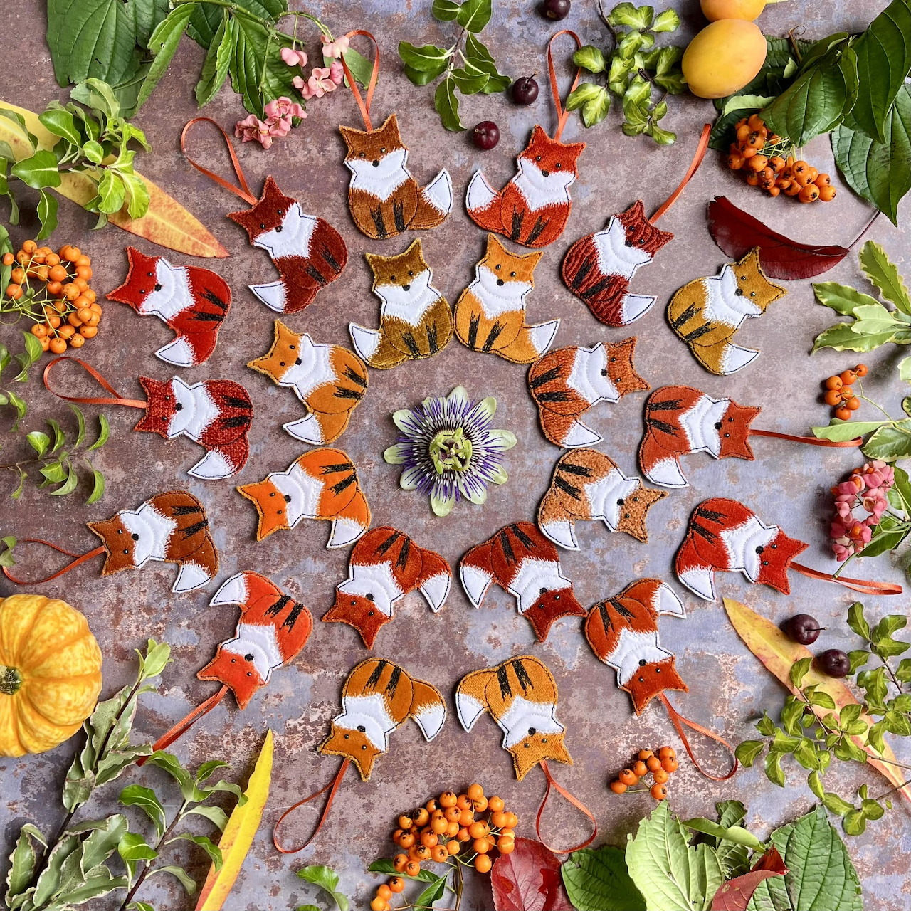 Radial mandala pattern made of autumn leaves, orange berries, purple flowers, and small pumpkins arranged symmetrically