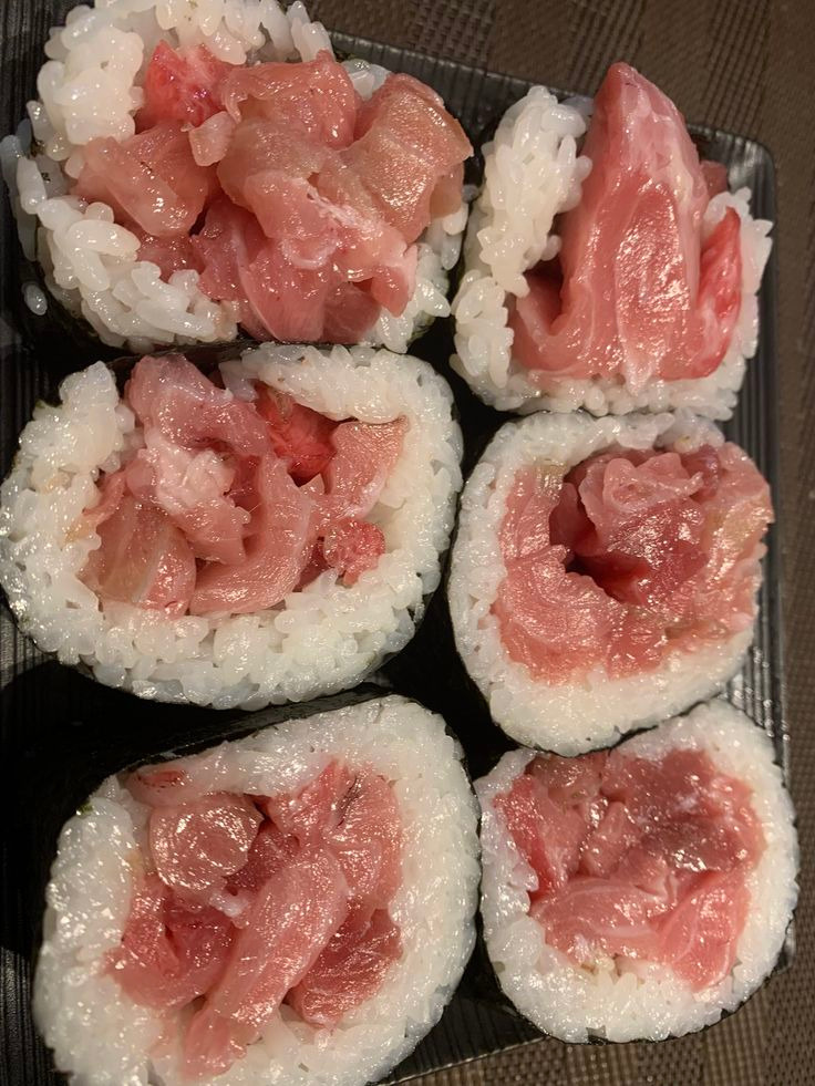 Six tuna sushi rolls with rice and raw tuna on dark plate