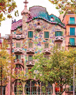 Colorful mosaic facade of Casa Batlló with curved balconies and decorative roof surrounded by trees