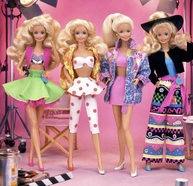 Four Barbie dolls wearing colorful retro fashion outfits on a pink background