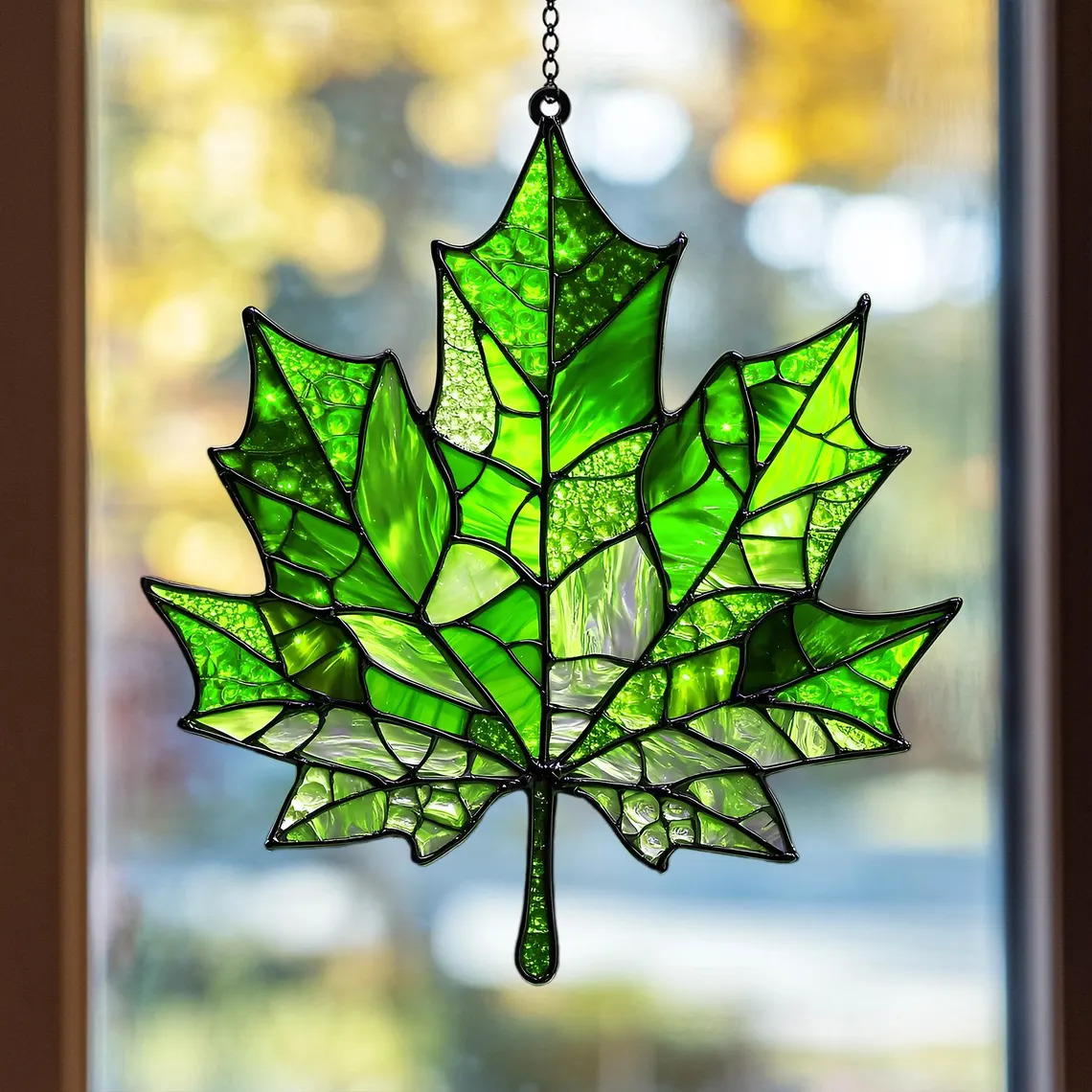 Green leaf suncatcher hanging in a window with blurred background