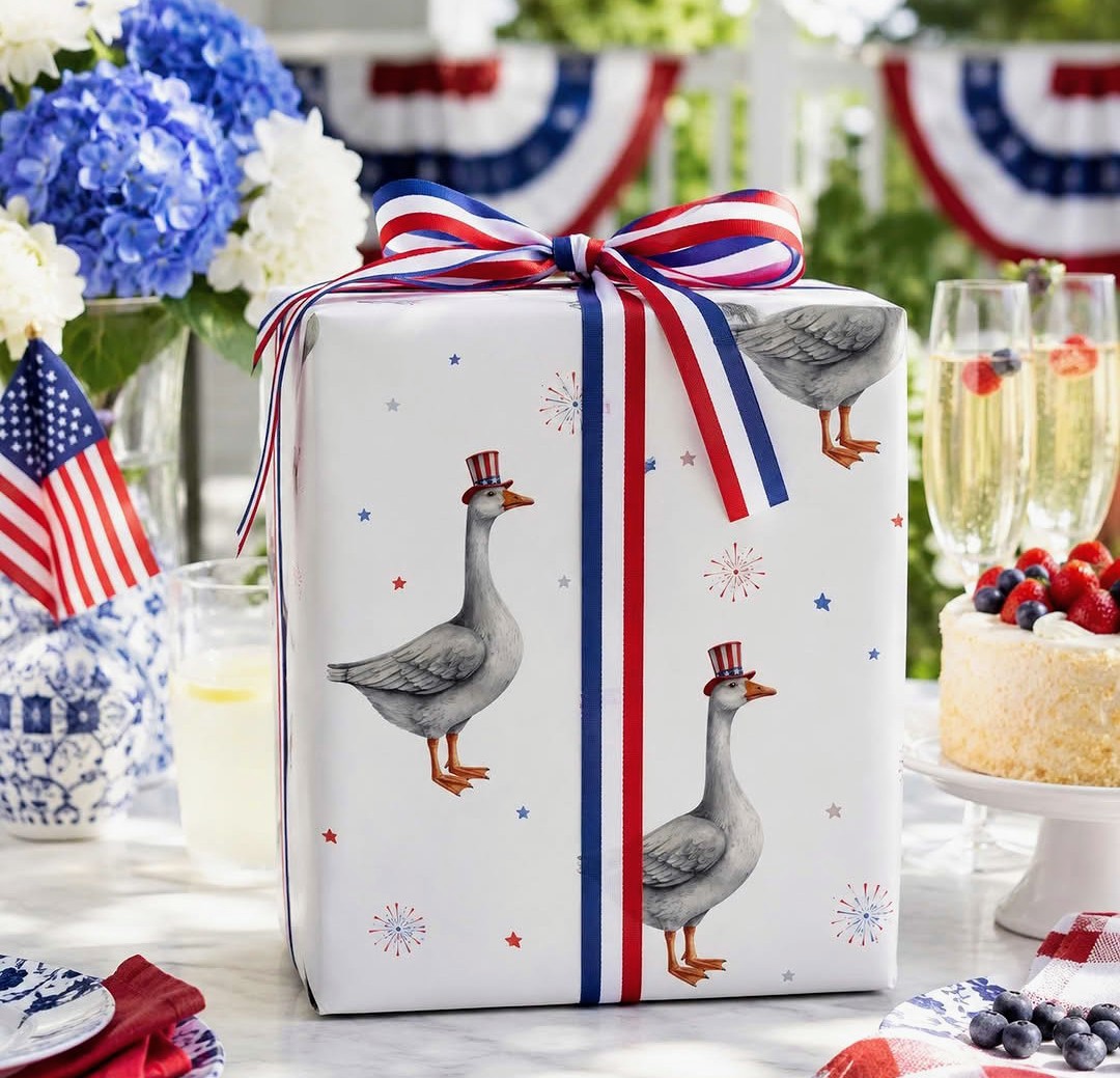 Patriotic gift box with red, white, and blue ribbon on a party table with flowers, cake, and berries