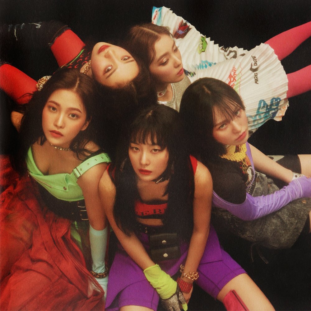 Four women in colorful clothing pose closely together against a dark background