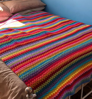 Colorful rainbow striped crochet blanket on bed with brown and blue pillows