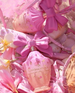 Pink perfume bottle with satin bows, seashells, and plumeria flowers on sandy background