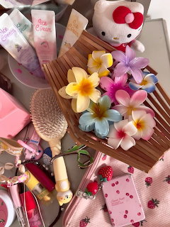 Flat lay of frangipani flowers on wooden tray with pink beauty products, Hello Kitty plush, and girly accessories
