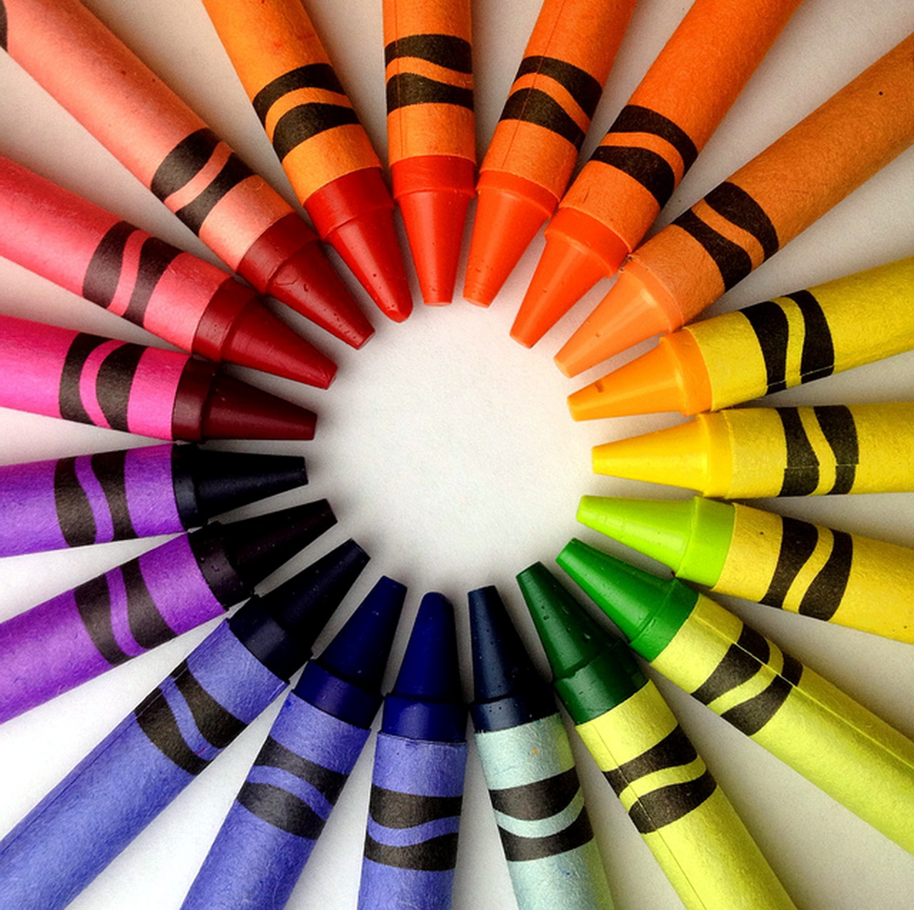 Crayons arranged in a circular rainbow color wheel pattern on white background