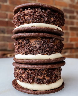 Three stacked chocolate ice cream sandwiches with vanilla filling on white surface and brick wall background
