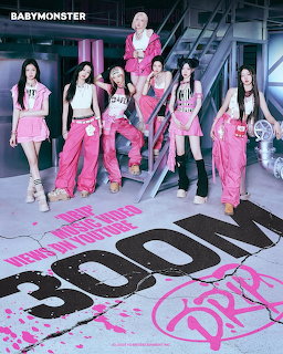 Six women in pink outfits posing in an industrial set with large BABYMONSTER floor text