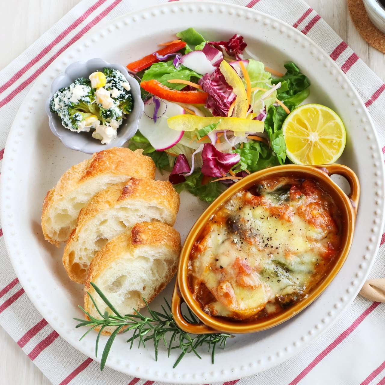 Plate with sliced baguette, baked casserole, mixed salad, cottage cheese bowl, and lemon slices