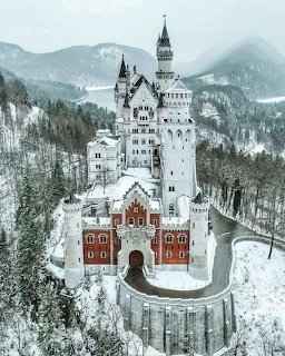 Neuschwanstein Castle in winter with snow-covered forests and mountain backdrop