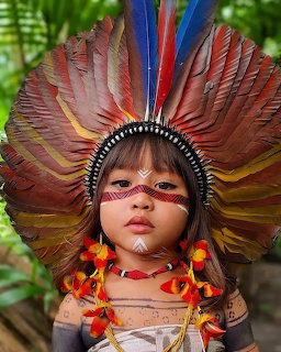 Young child in a large feather headdress with face paint and colorful tassels outdoors