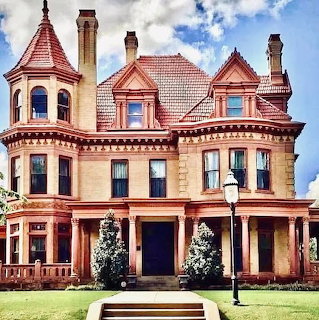 Large Victorian house with turrets, porch columns, and a lamp post in front