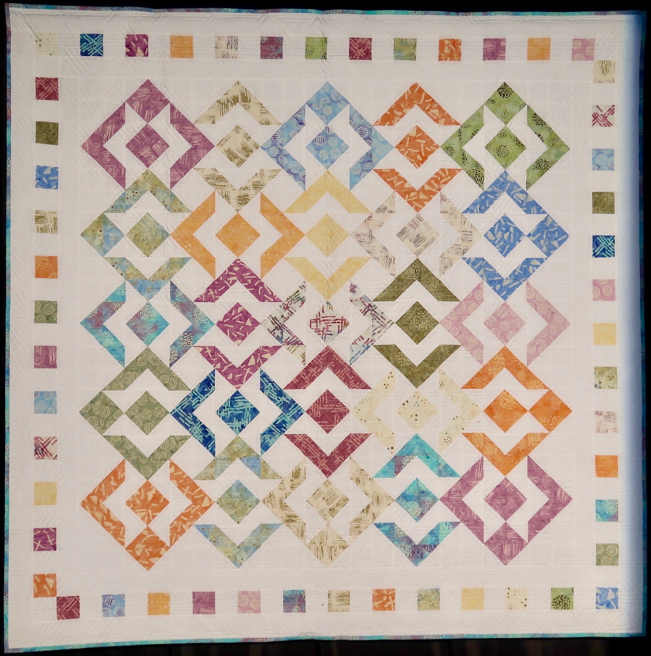 Colorful patchwork quilt with geometric diamond patterns in rainbow colors on cream fabric with multicolored square border
