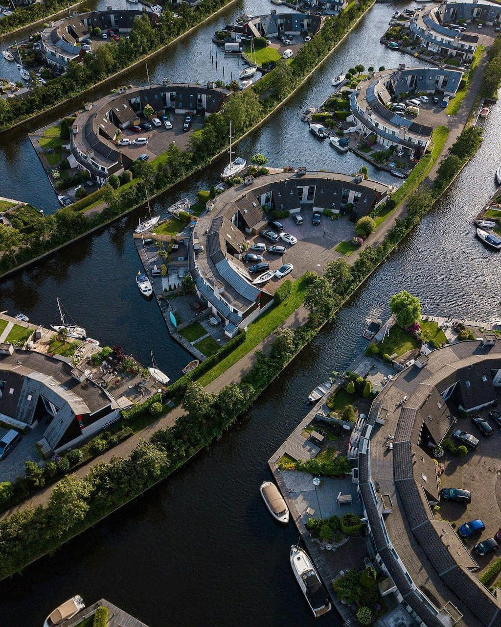 Aerial view of curved residential streets with canals and boats in a Dutch waterfront neighborhood