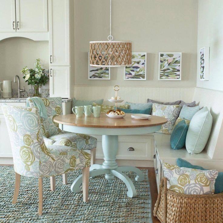 Coastal dining nook with round table, blue cushioned bench seating, and floral accent chairs