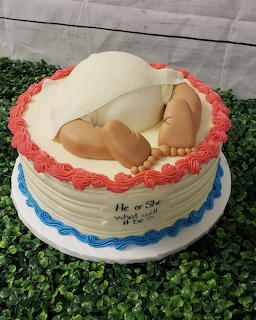 White frosted cake with pink roses and fondant baby decoration for gender reveal or baby shower celebration