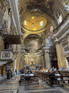 Ornate interior of a Rome church with arches, frescoes, statues, and wooden pews