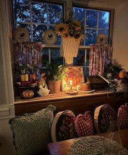 Cozy windowsill with sunflowers, candles, decorative plates, and houseplants in a cottage-style interior at dusk
